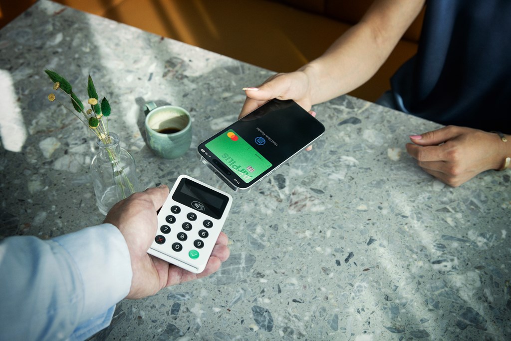 Kunde zahlt mit dem Handy und AirPlus Firmenkarte kontaktlos am Kartenterminal im Café.