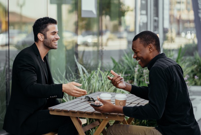 Two business payment partners sitting at a coffee shop bench talking and laughing