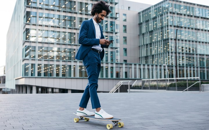 A business traveler on a skateboard while checking transaction data using mobile phone outside an office block