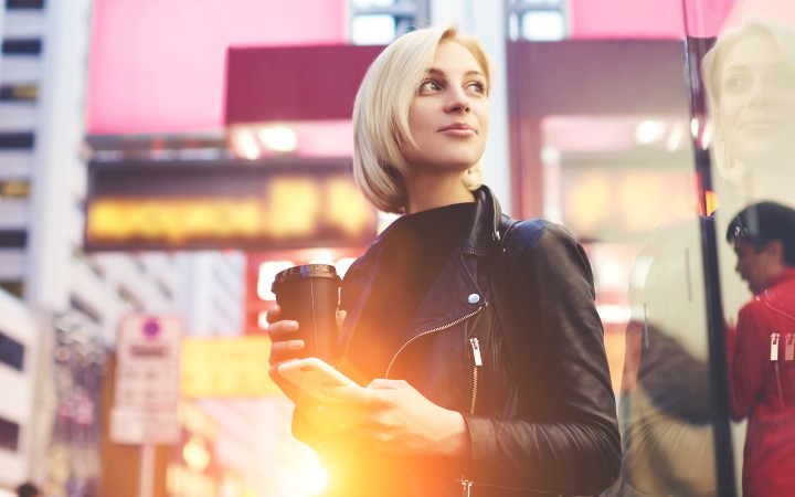 Traveler in city with coffee and mobile phone in hand calling travel agent
